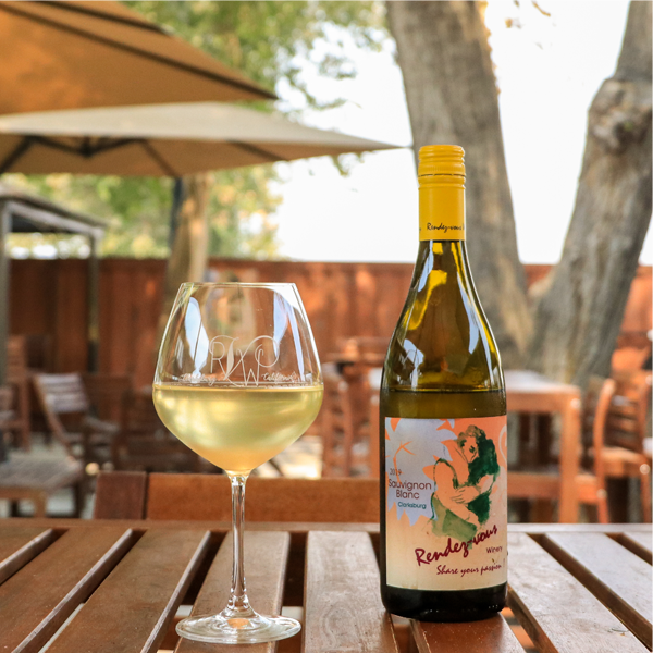 A1: Bottle of Rendez-vous Winery Sauvignon Blanc wine with a glass on a wooden table outdoors.