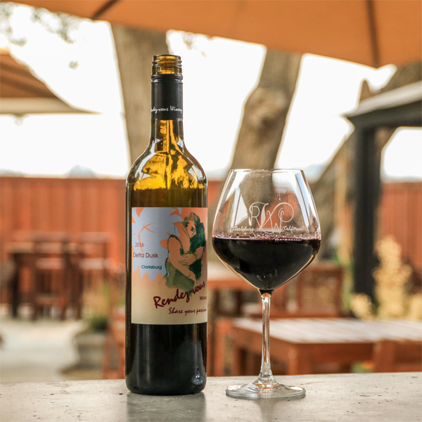 Wine bottle and glass of red wine on an outdoor table at Rendez-vous Winery.